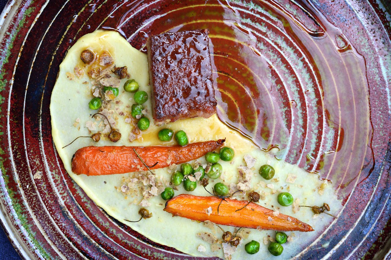 Elegant presentation of glazed carrots, peas, and beef on a textured plate.