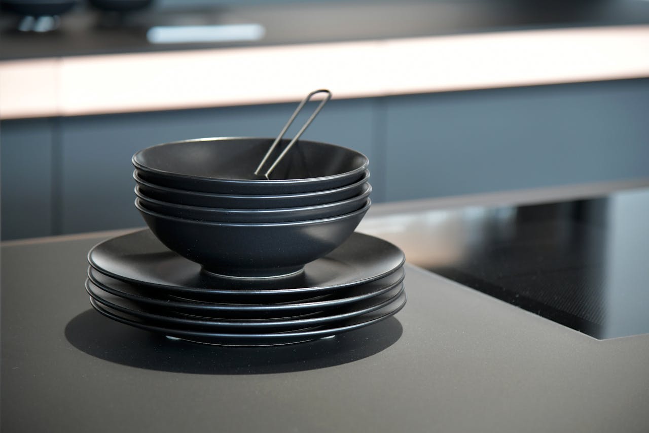 Stack of black dinnerware with bowl and plates in a modern kitchen, San Martino Buon Albergo.